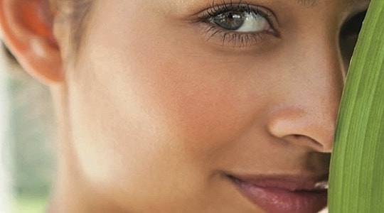 Woman peeking behind a green leaf.