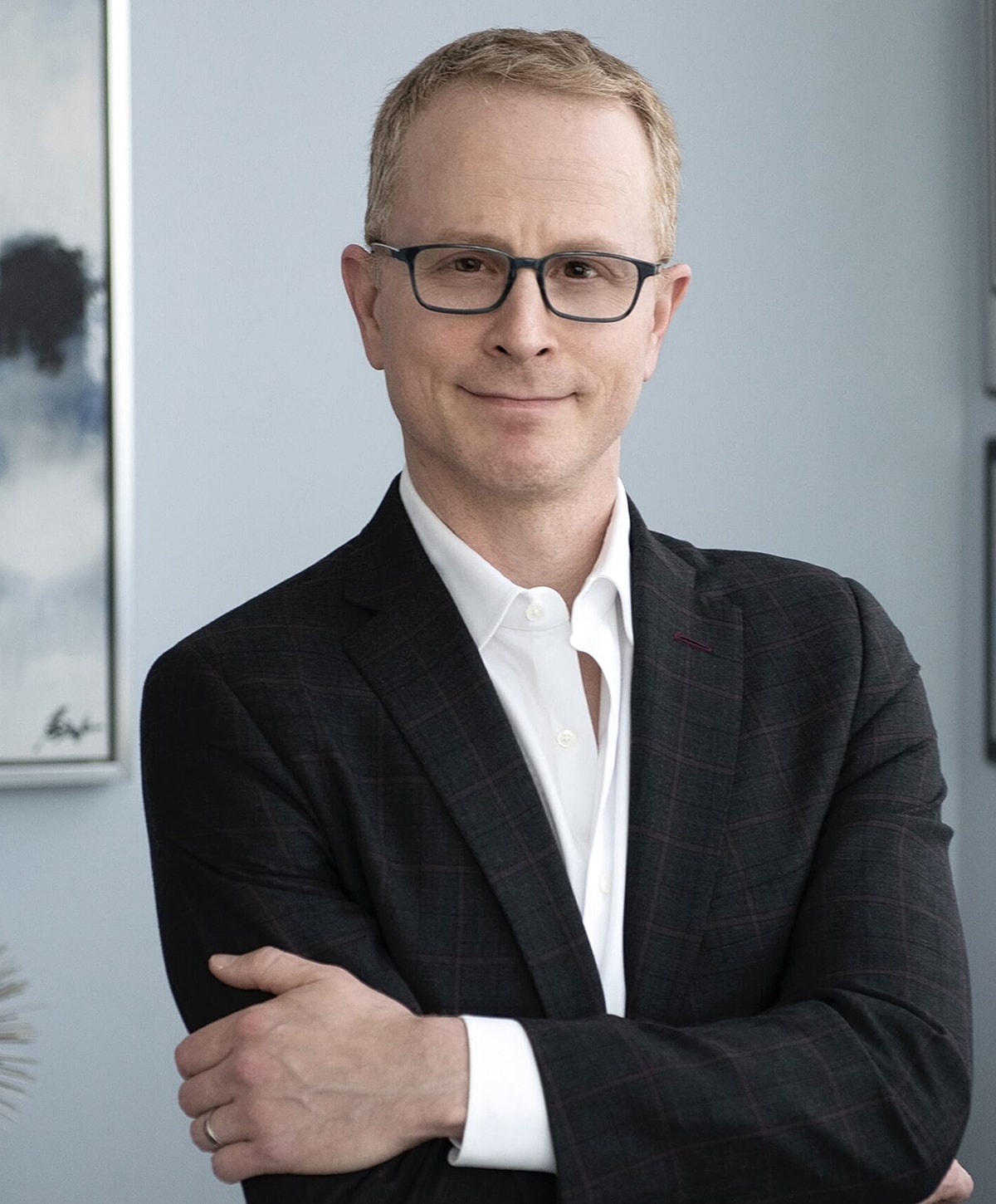 Man with glasses wearing a suit, smiling confidently.