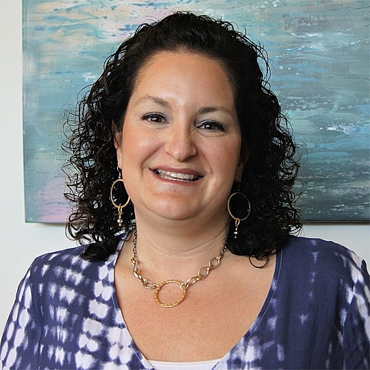 Smiling woman with curly hair and jewelry.