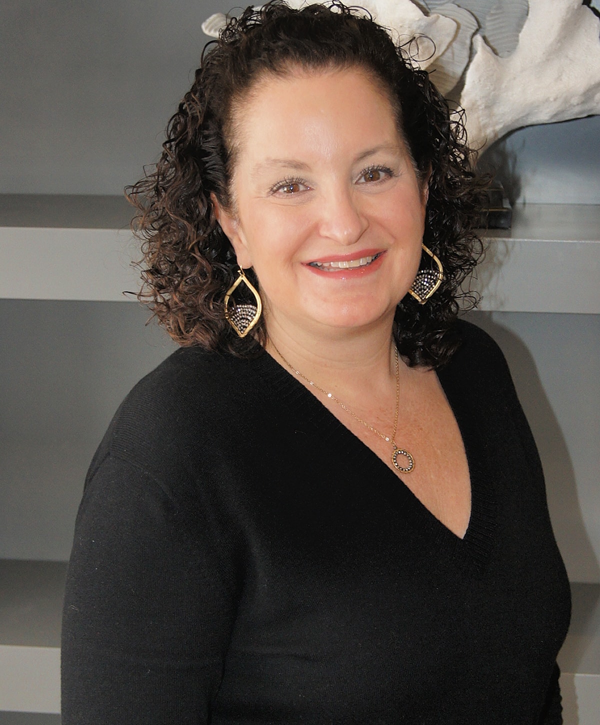 Woman smiling in black sweater, with jewelry.
