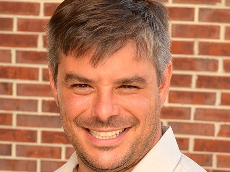 Smiling man against a brick wall background.