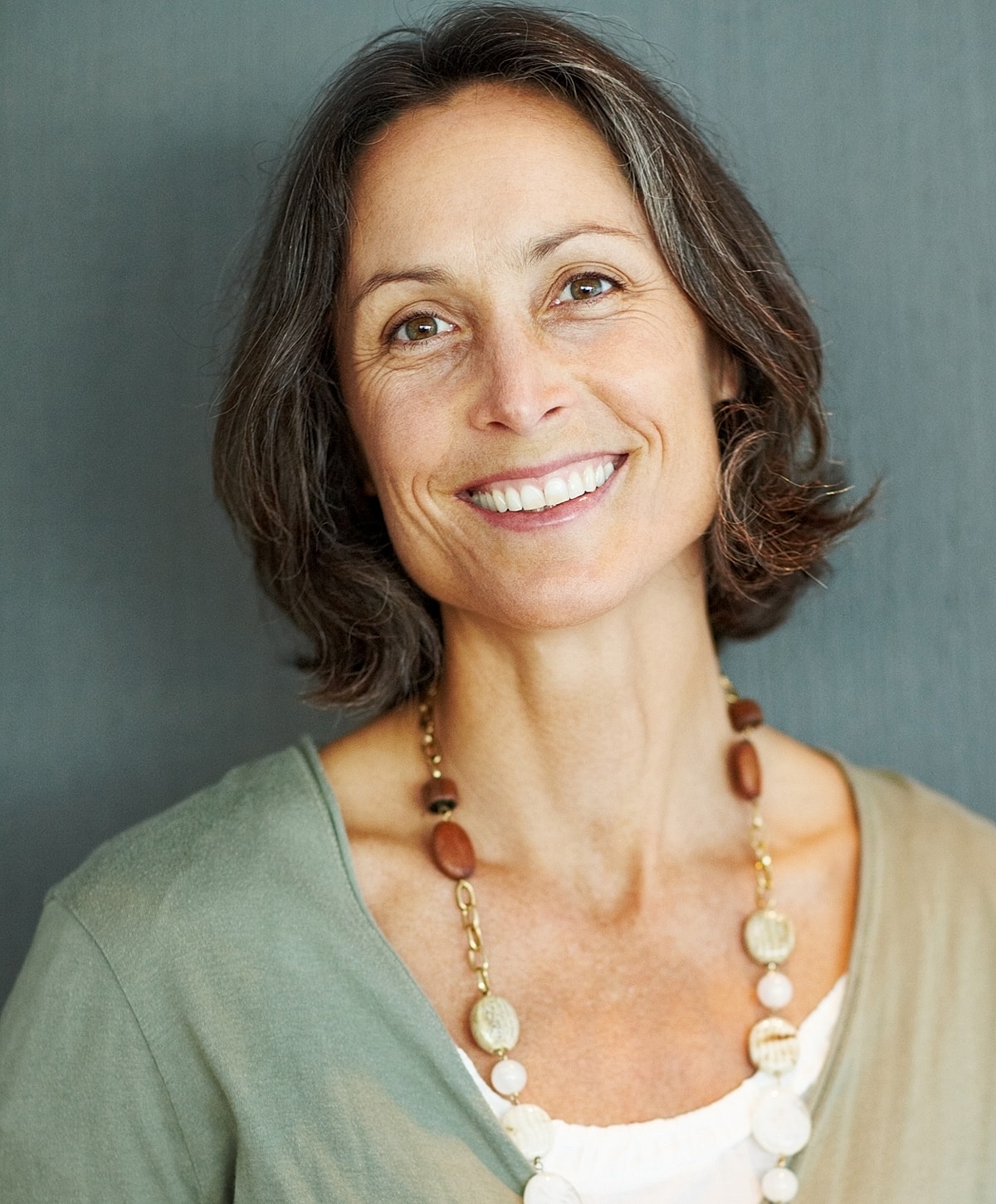 Smiling woman wearing a necklace, neutral background.
