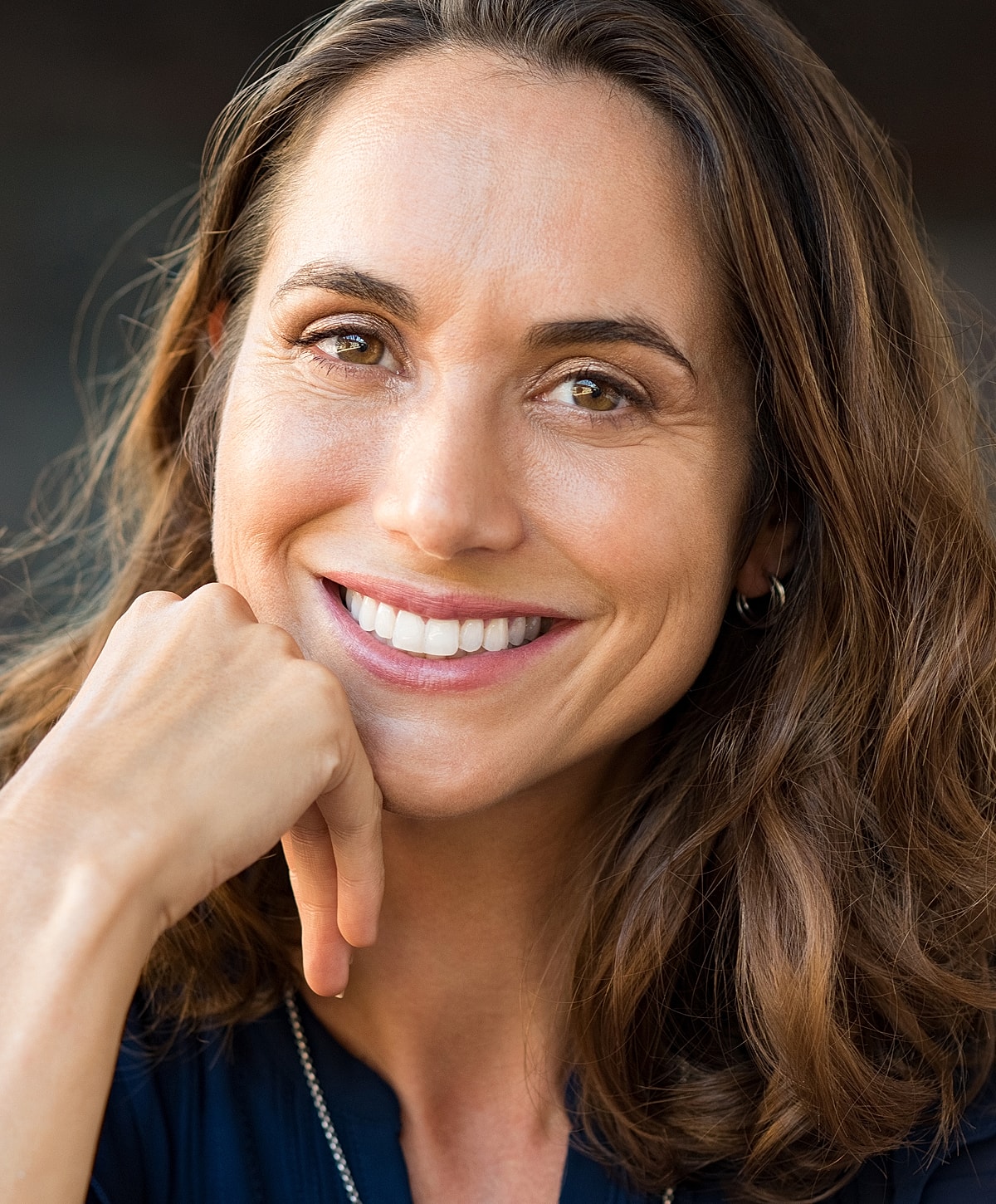 Smiling woman with long hair, hand on chin.