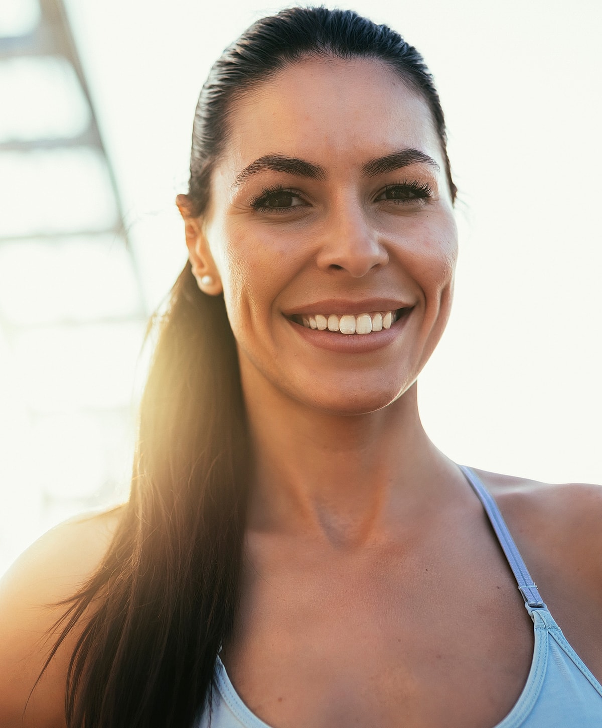 Smiling woman outdoors, sunlit background.