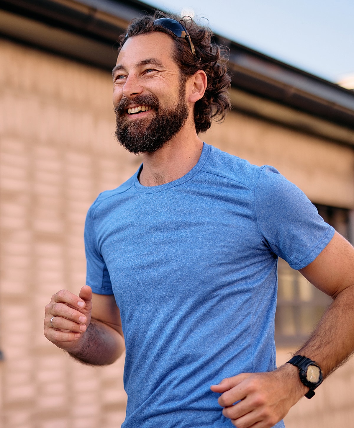 Smiling man jogging outdoors in a blue shirt.