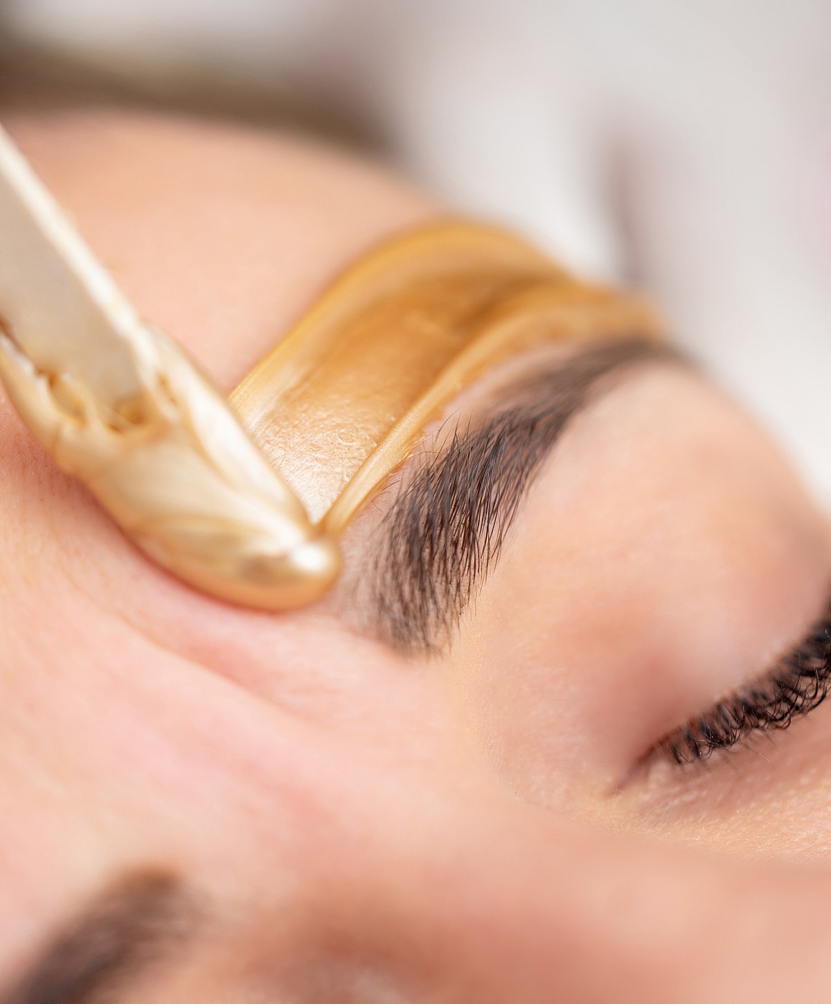 Eyebrow waxing process close-up on skin.