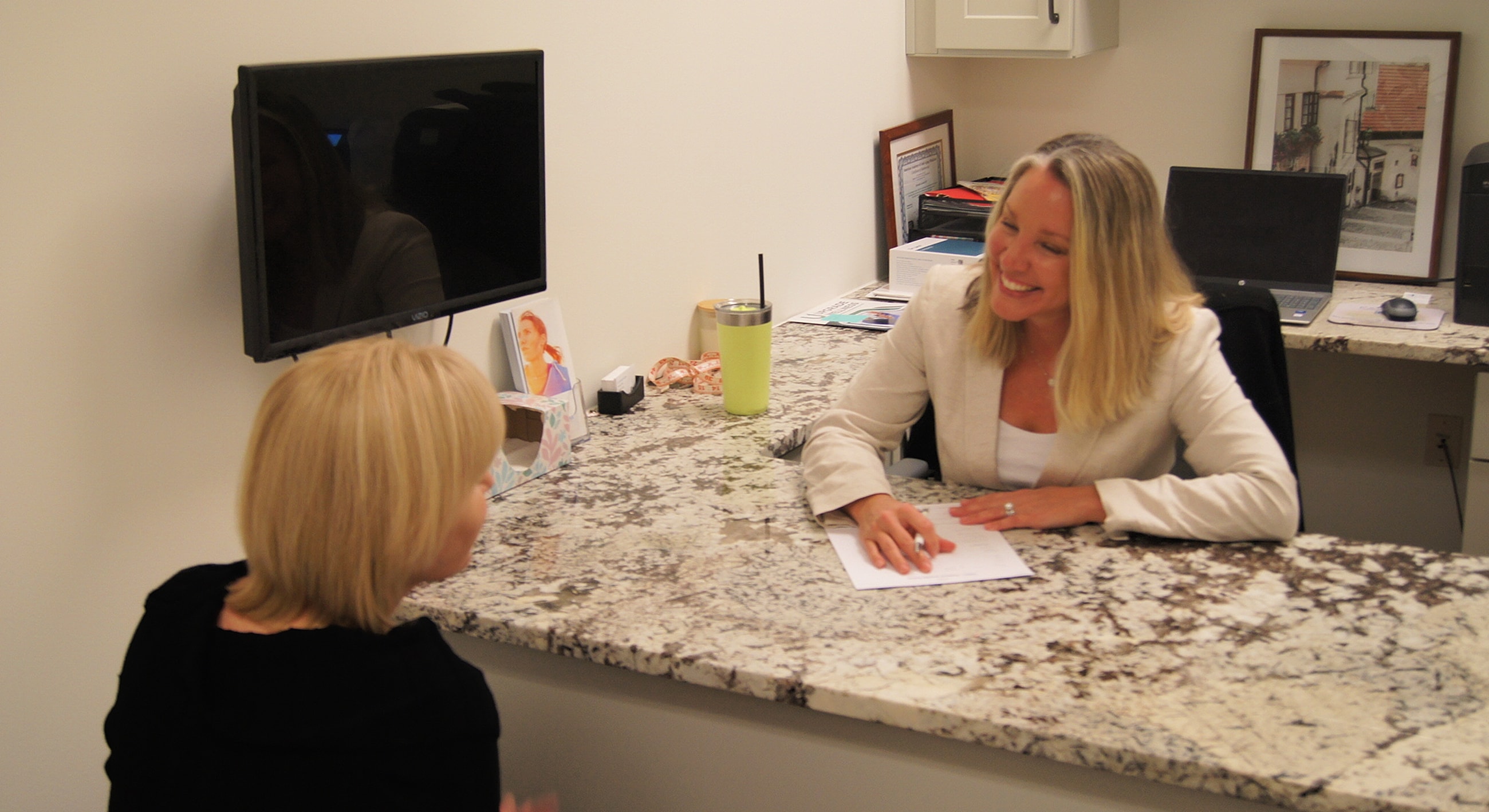 Two women discussing at an office reception desk.