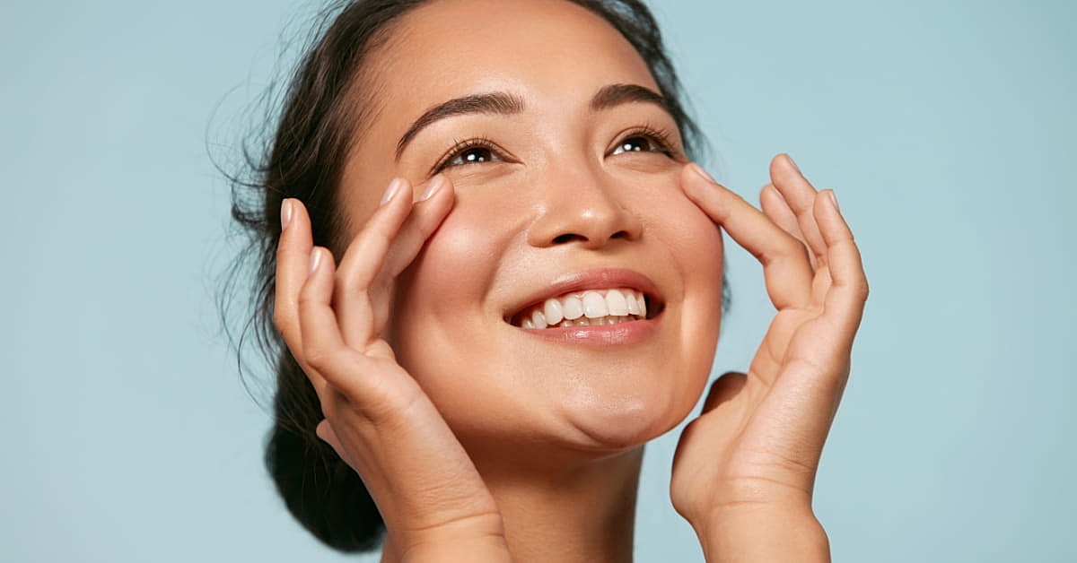 Woman with clear skin smiling while lightly touching her under eye area