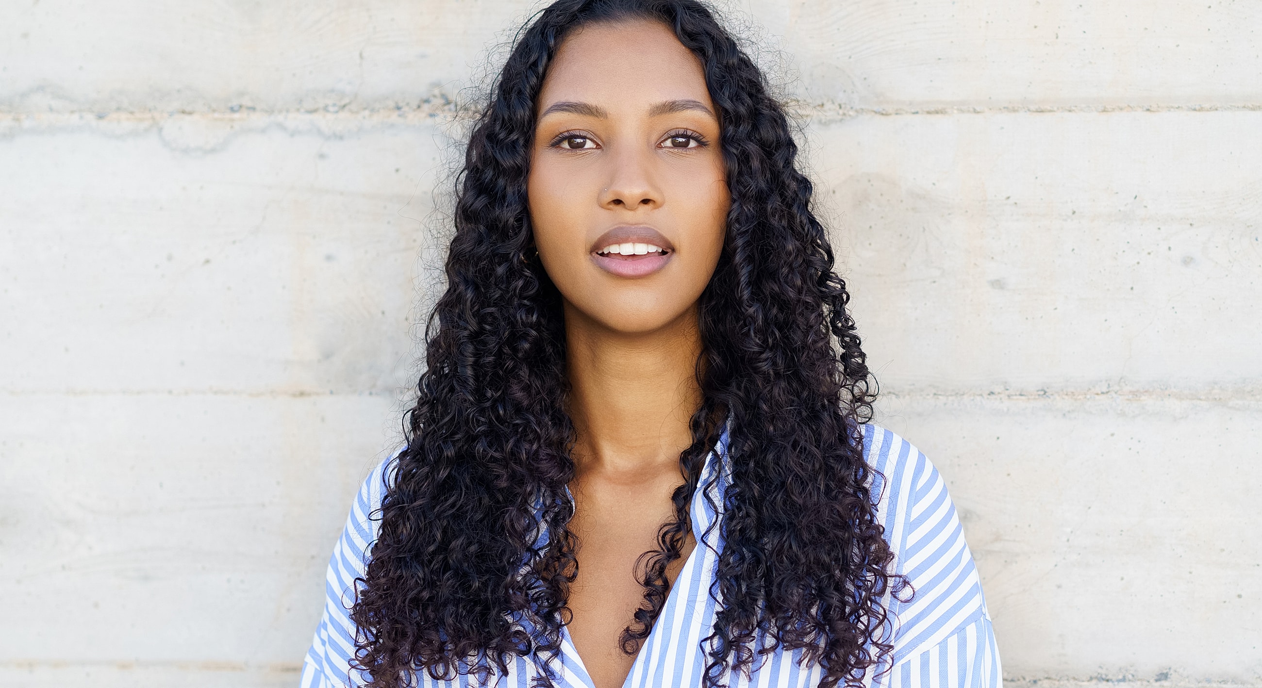 Smiling woman with curly hair against textured wall.