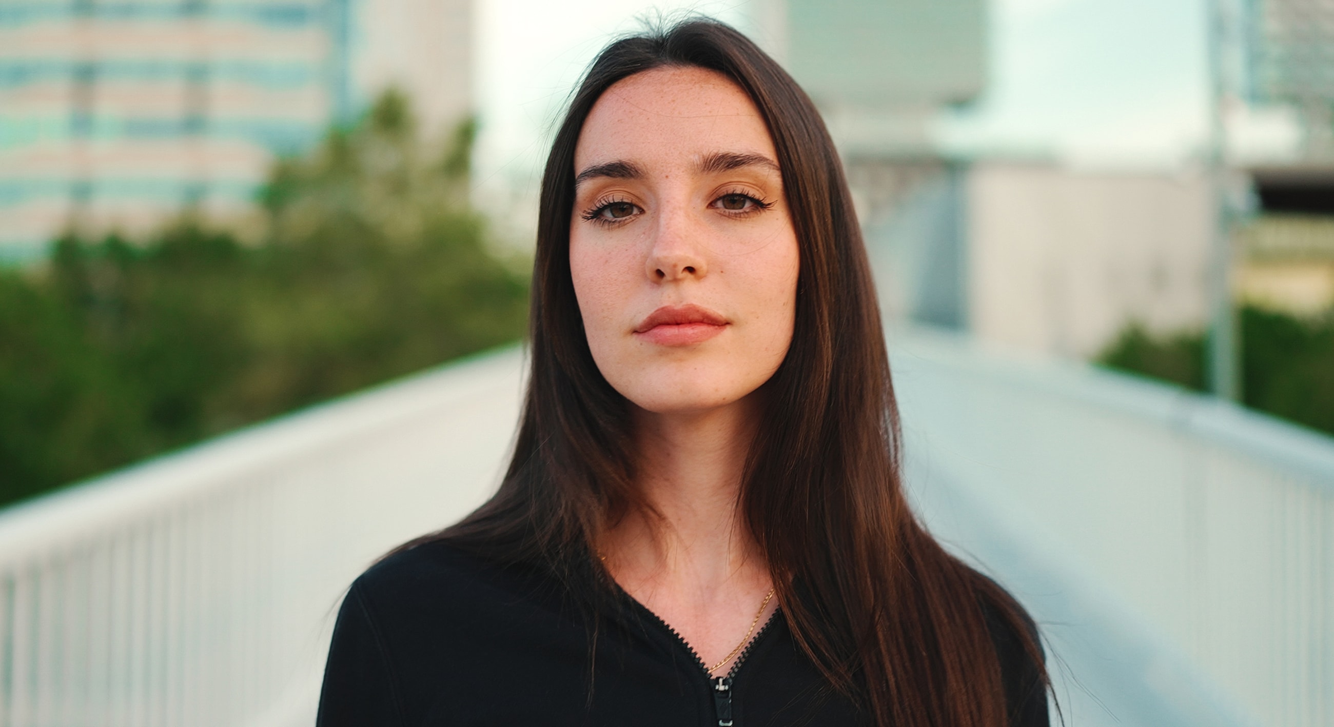 Young woman with long hair outdoors, serious expression.