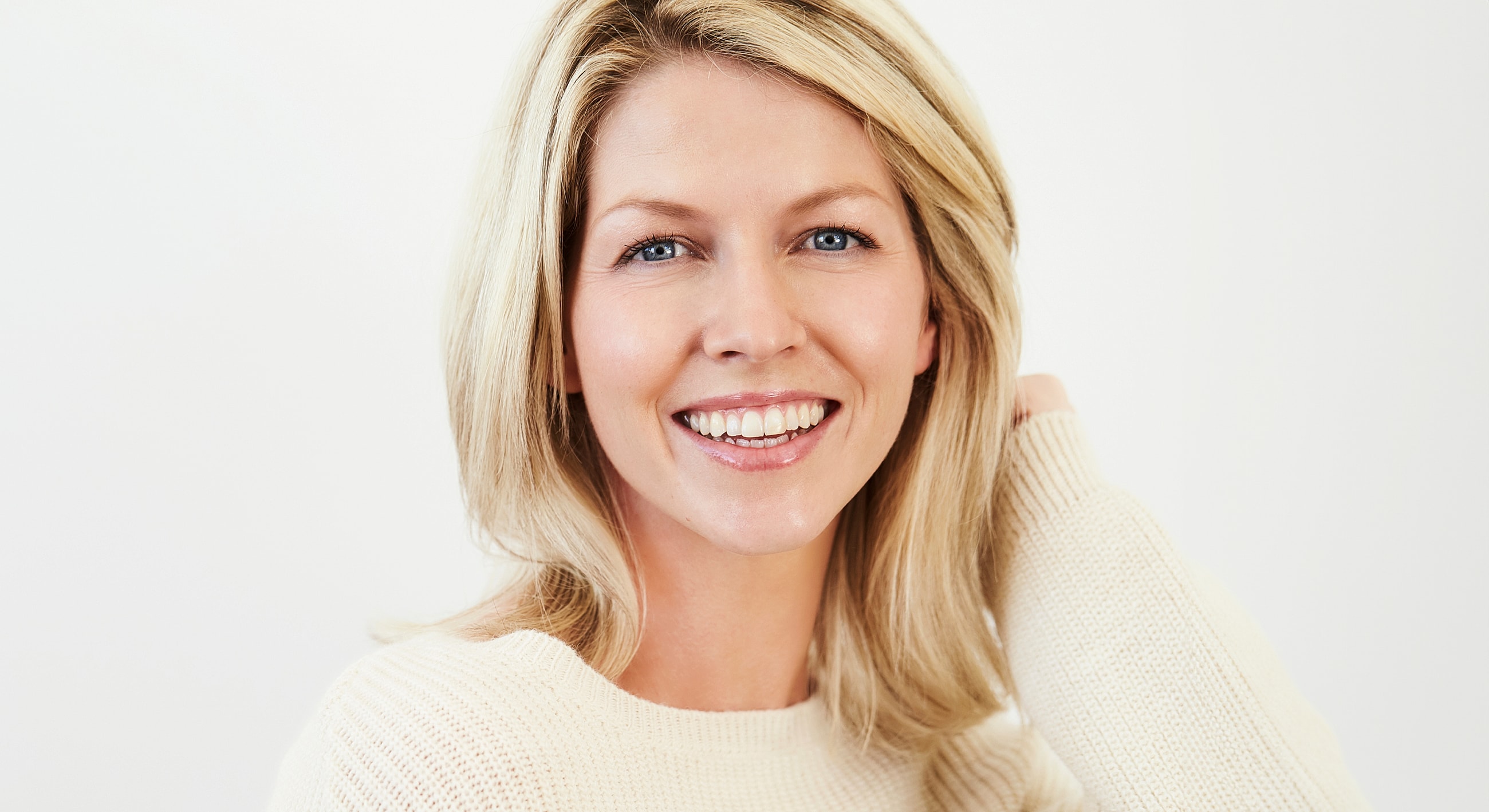 Smiling woman with blonde hair in cream sweater.