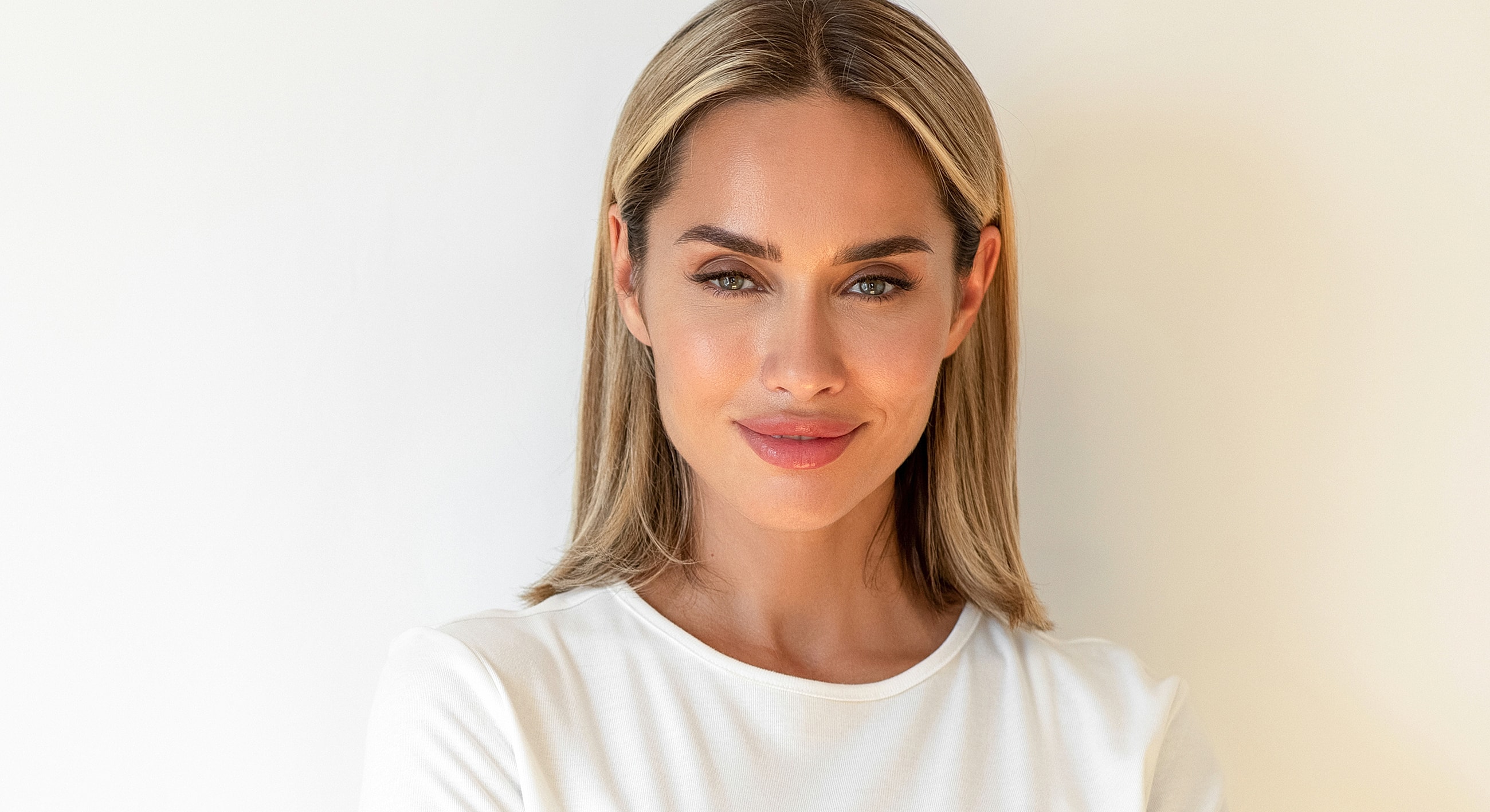 Smiling woman in white shirt against neutral background.
