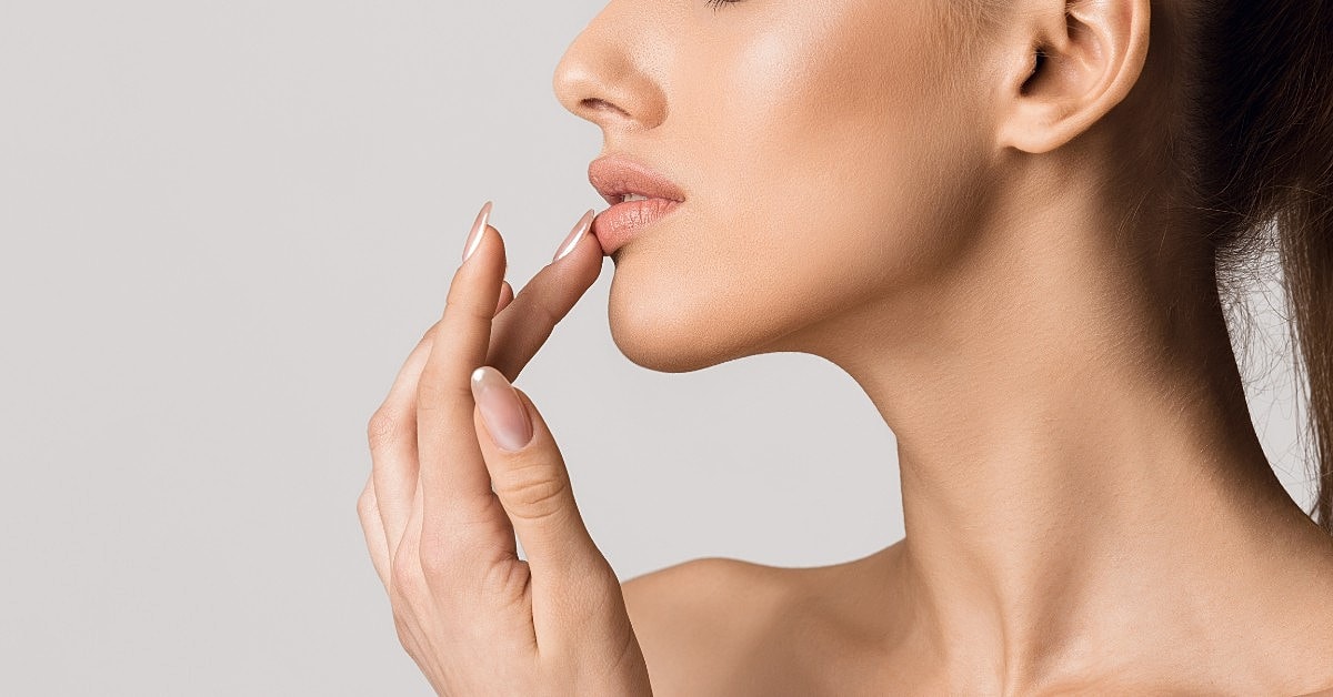Woman touching her full, naturally enhanced lips after a lip filler treatment