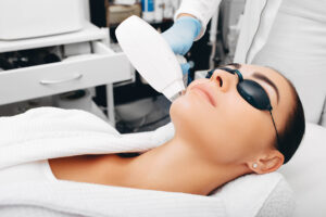 At Ageless Remedies of Roswell clinic, a woman receives BroadBand Light Therapy on her face, wearing protective goggles as a specialist uses the BBL device.